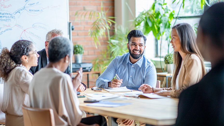 Imagem com uma sala de reuniões como fundo e um grupo de colaboradores felizes debatendo ações de Sustentabilidade Corporativa.